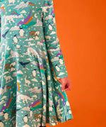 Close up of the side of the Frugi GOTS organic cotton sofia skater dress in polar aurora showing the flared skirt. Blue green background with and all over print featuring polar animals among star and colourful swishes. 