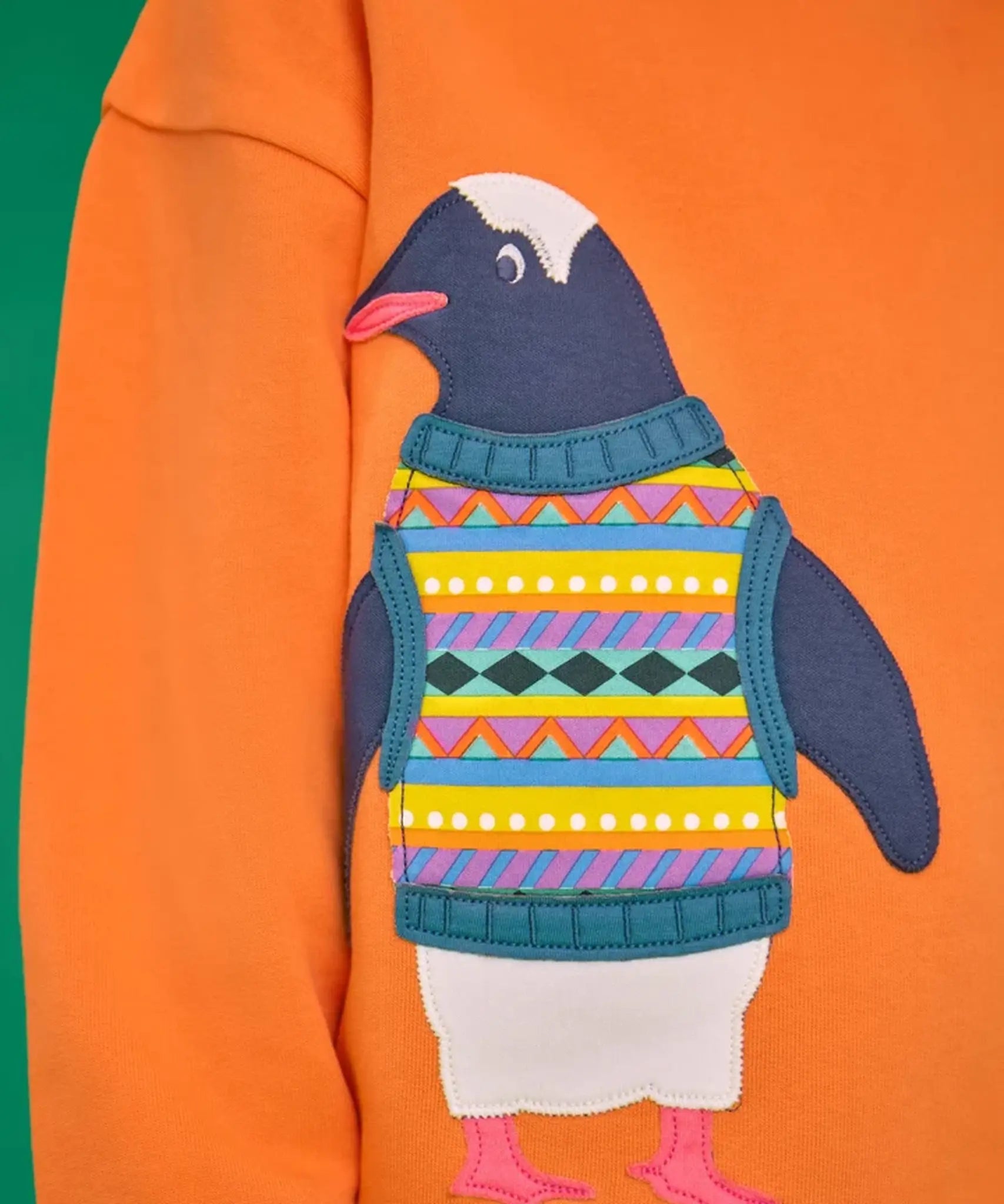 Close up of the penguin applique on the Frugi organic cotton superb sweatshirt salamander orange.