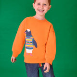 Child wearing the Frugi organic cotton superb sweatshirt salamander orange with penguin applique. The penguin is wearing a fairisle style tank top. 
