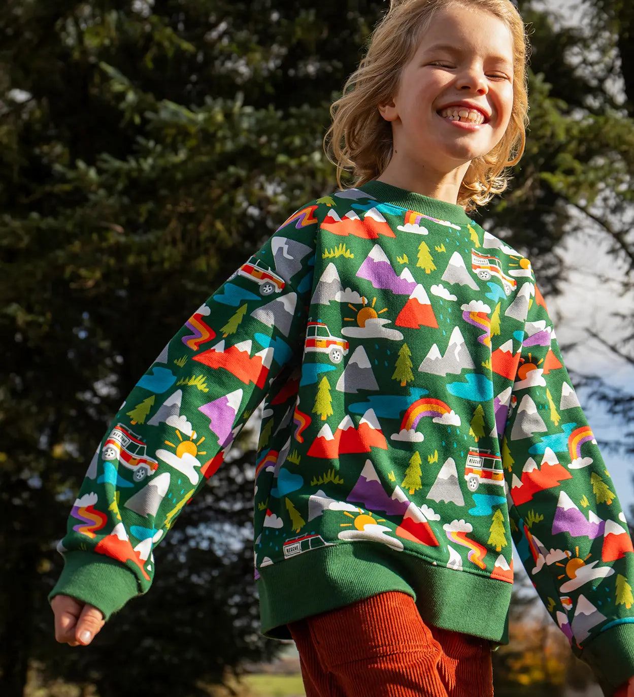 Child wearing the Frugi GOTS organic cotton superb sweatshirt with rescue trails print with rust orange corduroy trousers.