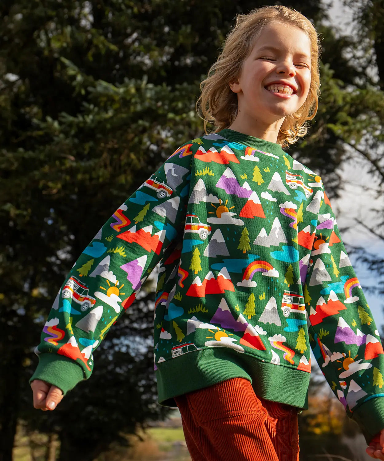 Child wearing the Frugi GOTS organic cotton superb sweatshirt with rescue trails print with rust orange corduroy trousers.