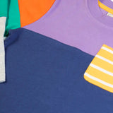 Close up of the  Frugi organic cotton kids long sleeved tregony hotchpotch top. Purple top with navy bottom with orange, teal and grey block colour sleeves with a yellow striped chest pocket. 