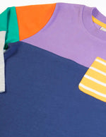 Close up of the  Frugi organic cotton kids long sleeved tregony hotchpotch top. Purple top with navy bottom with orange, teal and grey block colour sleeves with a yellow striped chest pocket. 