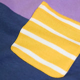 Close up of the yellow an dwhite striped chest pocket on the Frugi organic cotton kids long sleeved tregony hotchpotch top. Purple top with navy bottom with orange, teal and grey block colour sleeves.