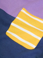 Close up of the yellow an dwhite striped chest pocket on the Frugi organic cotton kids long sleeved tregony hotchpotch top. Purple top with navy bottom with orange, teal and grey block colour sleeves.