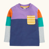 Frugi organic cotton kids long sleeved tregony hotchpotch top. Purple top with navy bottom with orange, teal and grey block colour sleeves with a yellow striped chest pocket. 