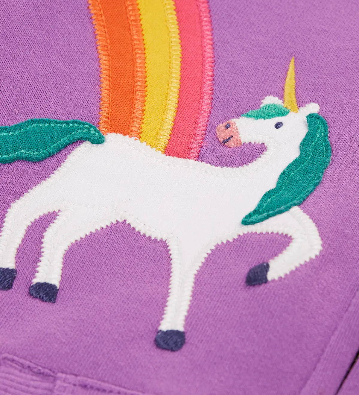 Close up of the unicorn and rainbow appliques on the front of the Frugi organic cotton purple periwinkle carbis zipped children's hoodie. 