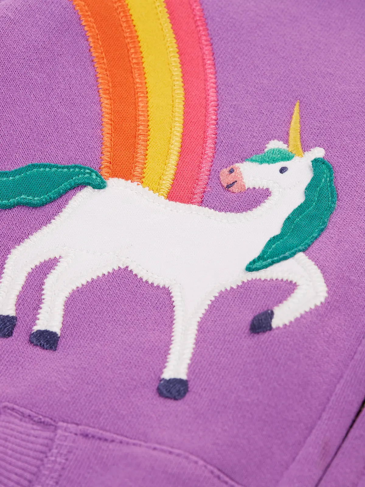 Close up of the unicorn and rainbow appliques on the front of the Frugi organic cotton purple periwinkle carbis zipped children's hoodie. 