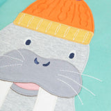 Close up of the large walrus wearing and orange bobble hat applique on the front of the Frugi organic cotton adventure circular long sleeved top in light moss green.