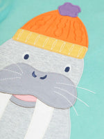 Close up of the large walrus wearing and orange bobble hat applique on the front of the Frugi organic cotton adventure circular long sleeved top in light moss green.