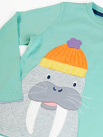 Close up of the Frugi organic cotton adventure circular long sleeved top in light moss green with a walrus wearing a bobble hat applique on the front. 