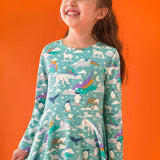 Child wearing the Frugi GOTS organic cotton sofia skater dress in polar aurora. Blue green background with and all over print featuring polar animals among star and colourful swishes. 