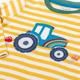 A close up of the tractor applique on the Frugi Orion Bumblebee tractor design long sleeved kids top. The tractor is blue with a rainbow on it's front and two red mushrooms either side of the tractor.