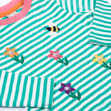 A close up of the embroidered  flower and bee details on the front of the Frugi Orion flowers long sleeved, organic cotton kids top. 
