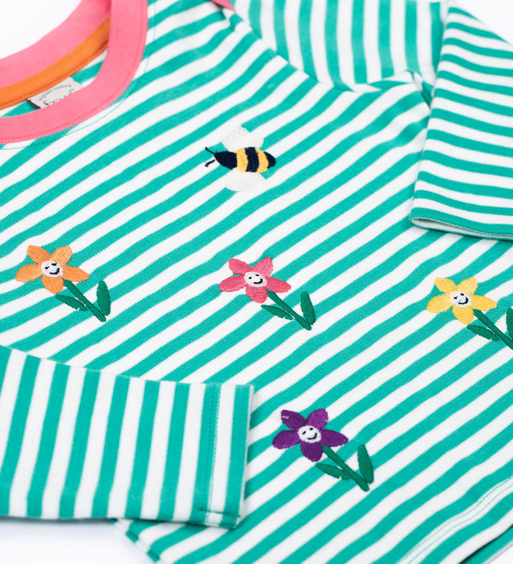 A close up of the embroidered  flower and bee details on the front of the Frugi Orion flowers long sleeved, organic cotton kids top. 