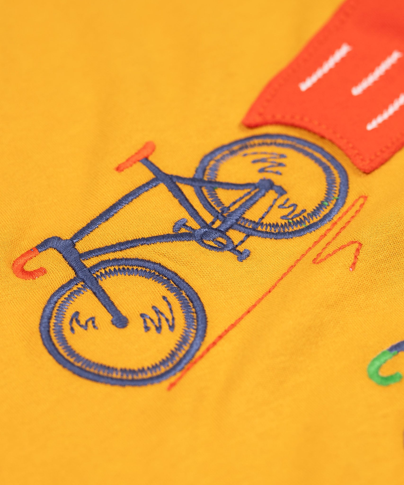 A super close up of the orange coloured embroidered bike on teh front of the Frugi Owen long sleeved child's top. 