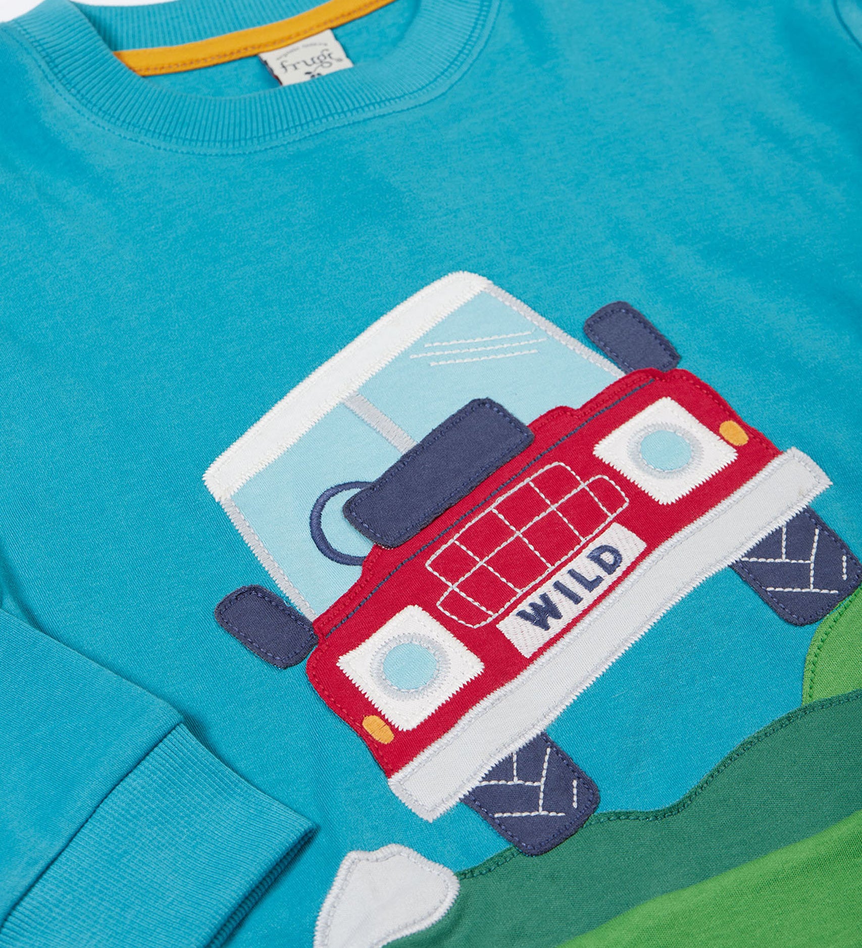 A close up of the red truck applique on the front of the Frugi Organic Cotton Owen Panel Circular Top in a Boat Blue colour with Truck design.
