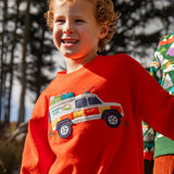 Child wearing the Frugi owen organic cotton long sleeved orange with a mountain rescue vehicle on the front. 