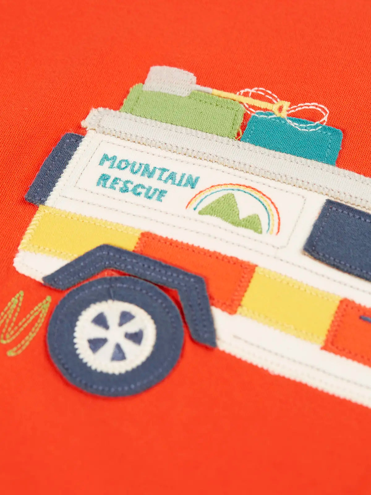 Close up of the white mountain rescue vehicle applique on the Frugi owen children's organic cotton long sleeved orange. 