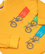 A close up of the embroidered and applique details on the front of the Frugi Owen top.  Three embroidered bicycles each with different coloured applique roads behind them.