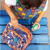 Child opening the Frugi explore the stars blue pack a lunch bag showing a repeating outer space design. Main and a small front compartment and a carry handle