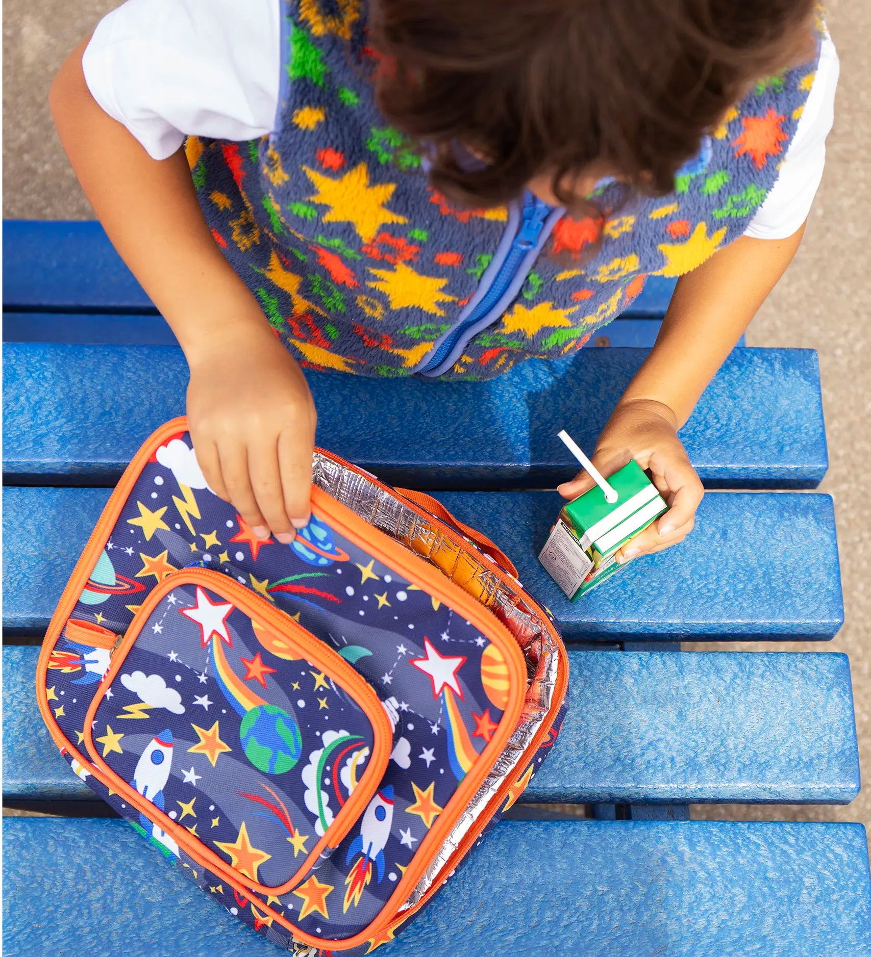 Child opening the Frugi explore the stars blue pack a lunch bag showing a repeating outer space design. Main and a small front compartment and a carry handle