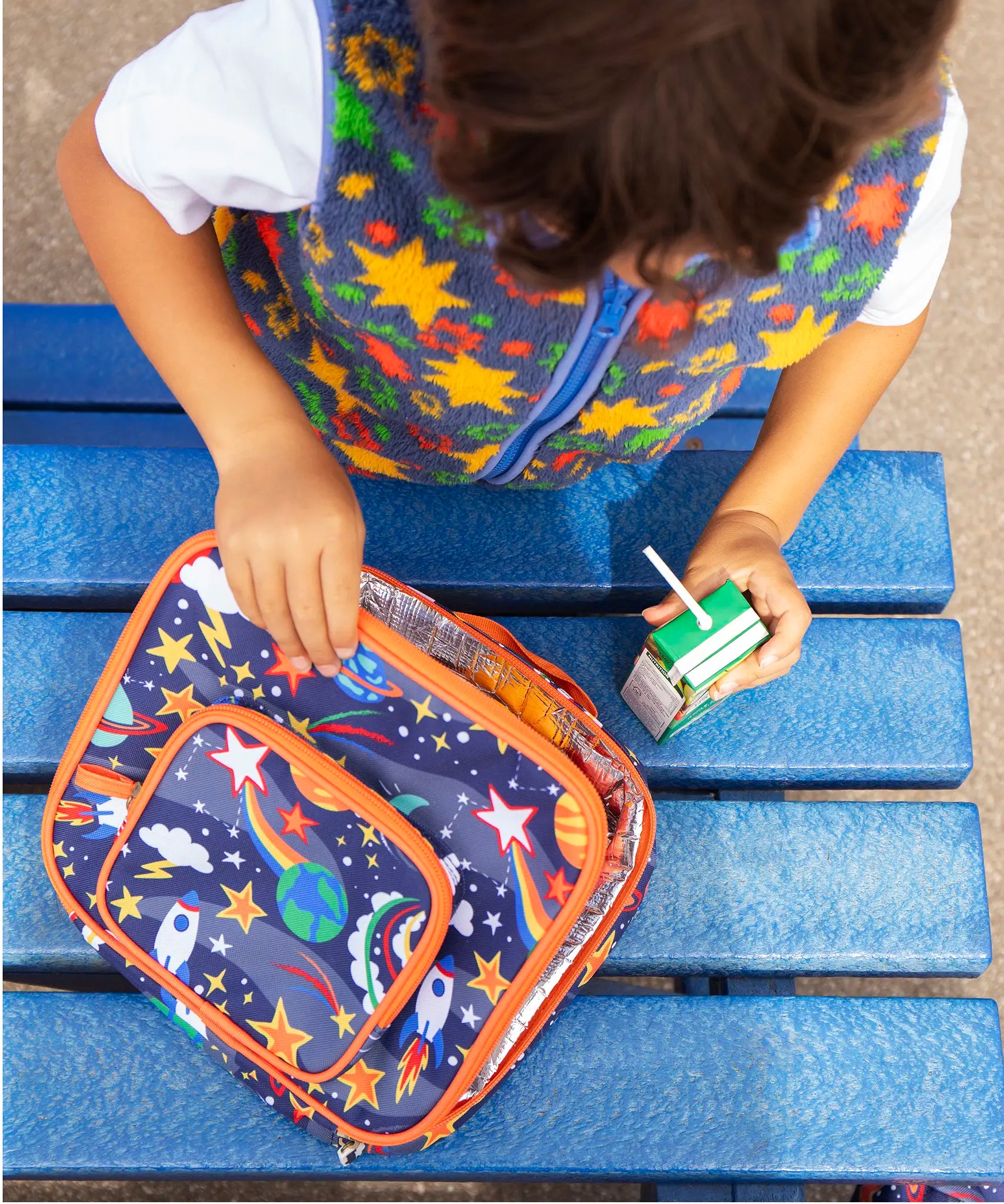 Child opening the Frugi explore the stars blue pack a lunch bag showing a repeating outer space design. Main and a small front compartment and a carry handle