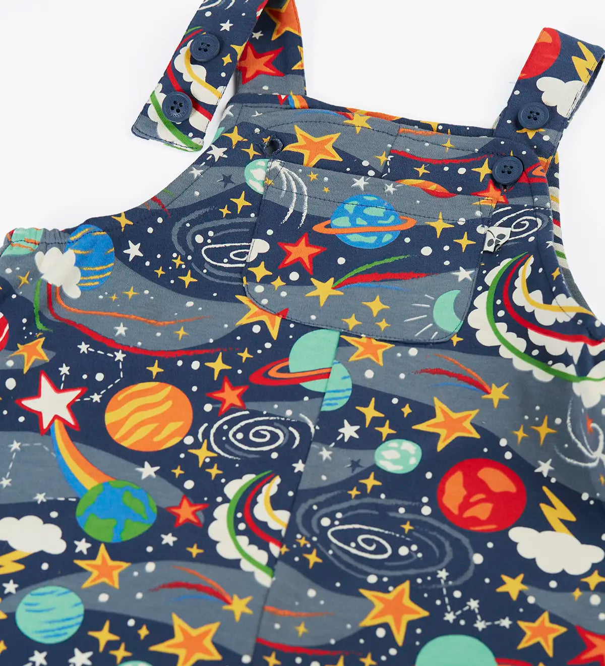 Close up of the button up straps and chest pocket on the front of the Frugi parsnip organic cotton dungaree in navy with an all over explore the stars print.