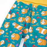 Frugi GOTS organic cotton parsnip pants in teal with a repeating guinea pig print and a yellow elasticated waistband for extender wear