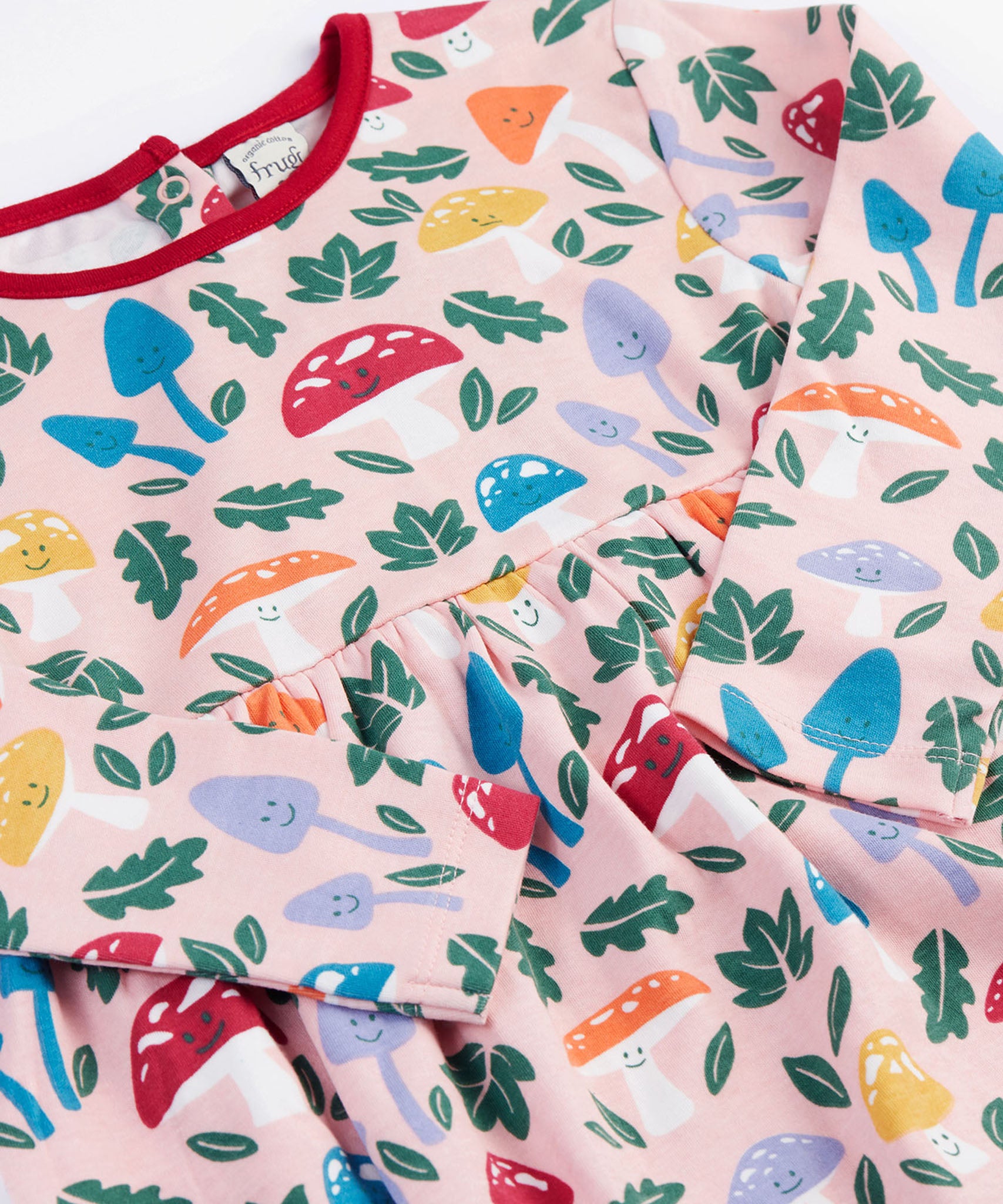 A close up of the Frugi kids pelican fun-guys amelia dress showing the playful woodland inspired print detail on pink organic cotton fabric.