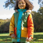 A child wearing the Frugi kids penhale Khaki parka outside- A long length thick warm coat  furry hood for warmth and  dark orange and yellow side pockets.