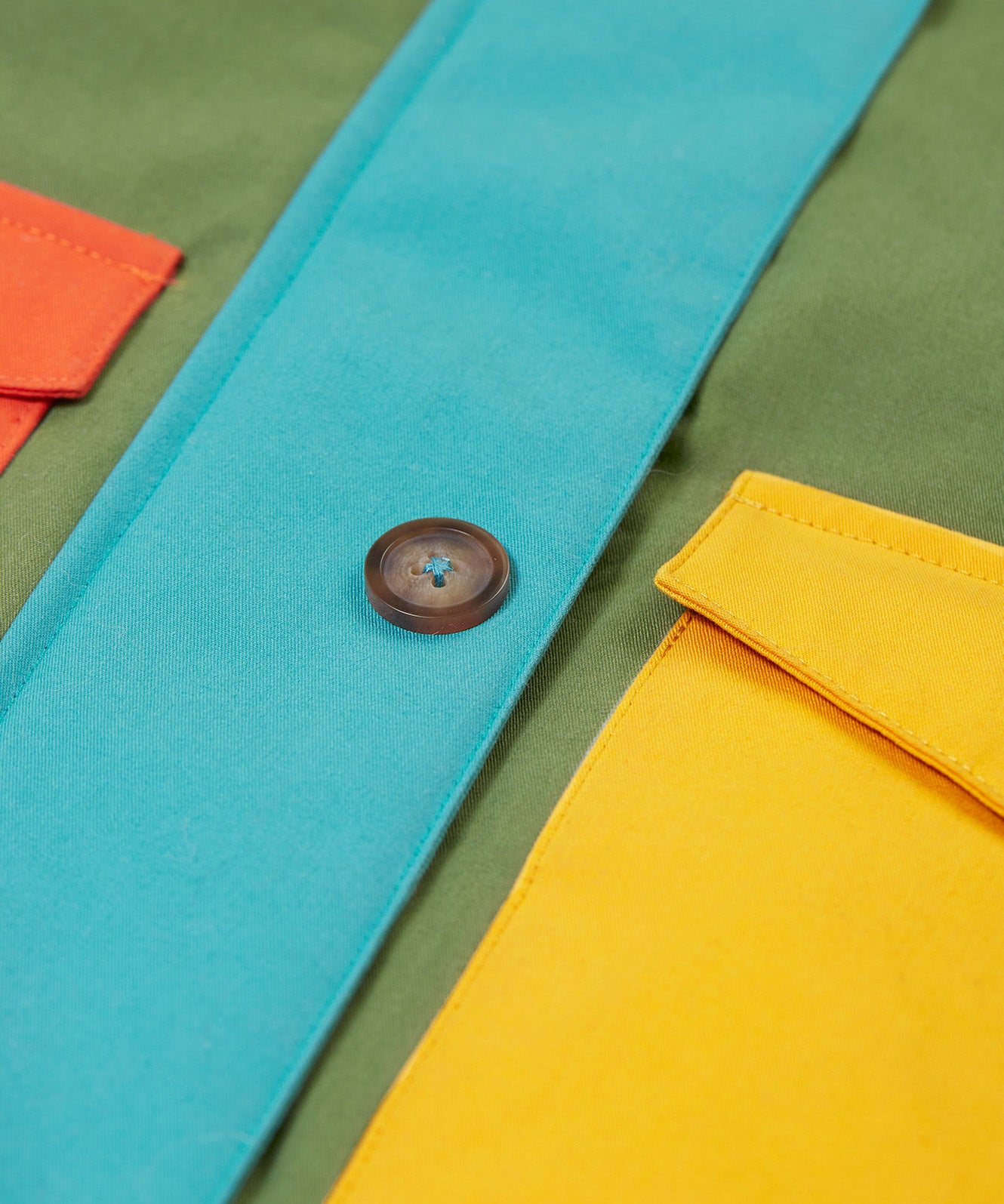 A close up of the Frugi khaki penhale colourblock parka showing the button fastener and pocket detail on organic cotton fabric