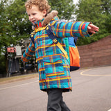 Child wearing Frugi's Penhale parka coat in a blue red and yellow tartan check with the faux fur trimmed hood down in a playground.