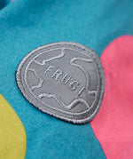 A close up of the orange arm of the Frugi super spot  parka showing the circular brand patch stitched on the top of the arm on organic cotton fabric