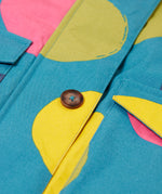 A close up of the Frugi khaki super spot  parka showing the button fastener and pocket detail on light blue organic cotton fabric