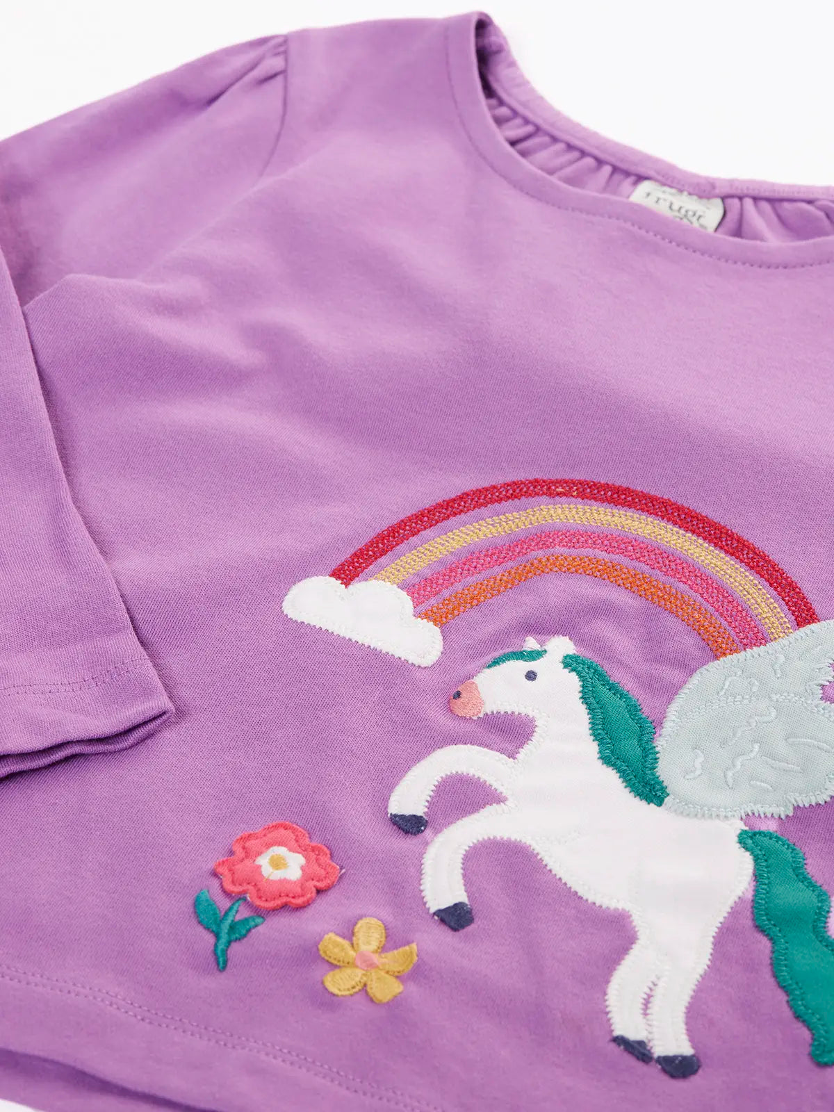 Close up of the front of the Close up of the white pegasus applique with rainbow and flowers details on the Frugi organic cotton periwinkle purple caris pegasus child's top. 