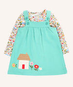 Frugi Pippa light moss green pinafore dress outfit with highland fields print long sleeved body. The light green dress has a highland house and floral applique detail on the front