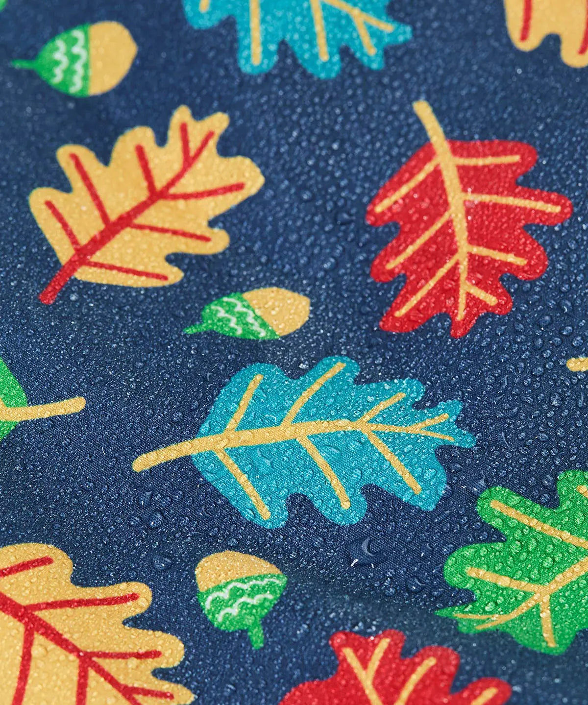 Frugi children's playtime waterproof coat with a multi-coloured acorn tumble print on a navy background, close up of water droplets formed on the material.