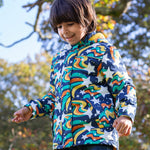 A toddler standing outside wearing the Frugi playtime magic stars coat. A thick long length hooded coat with a playful outer space inspired design