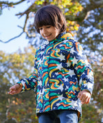 A toddler standing outside wearing the Frugi playtime magic stars coat. A thick long length hooded coat with a playful outer space inspired design