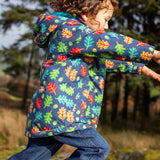 side of small child wearing the Frugi playtime waterproof coat in navy with a repeating multicoloured acorn design. Coat has a relaxed fit
