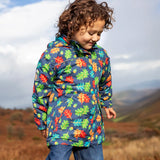 Small child wearing the Frugi playtime waterproof coat in navy with a repeating multicoloured acorn design. Showing the hood is down. 