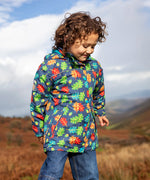 Small child wearing the Frugi playtime waterproof coat in navy with a repeating multicoloured acorn design. Showing the hood is down. 
