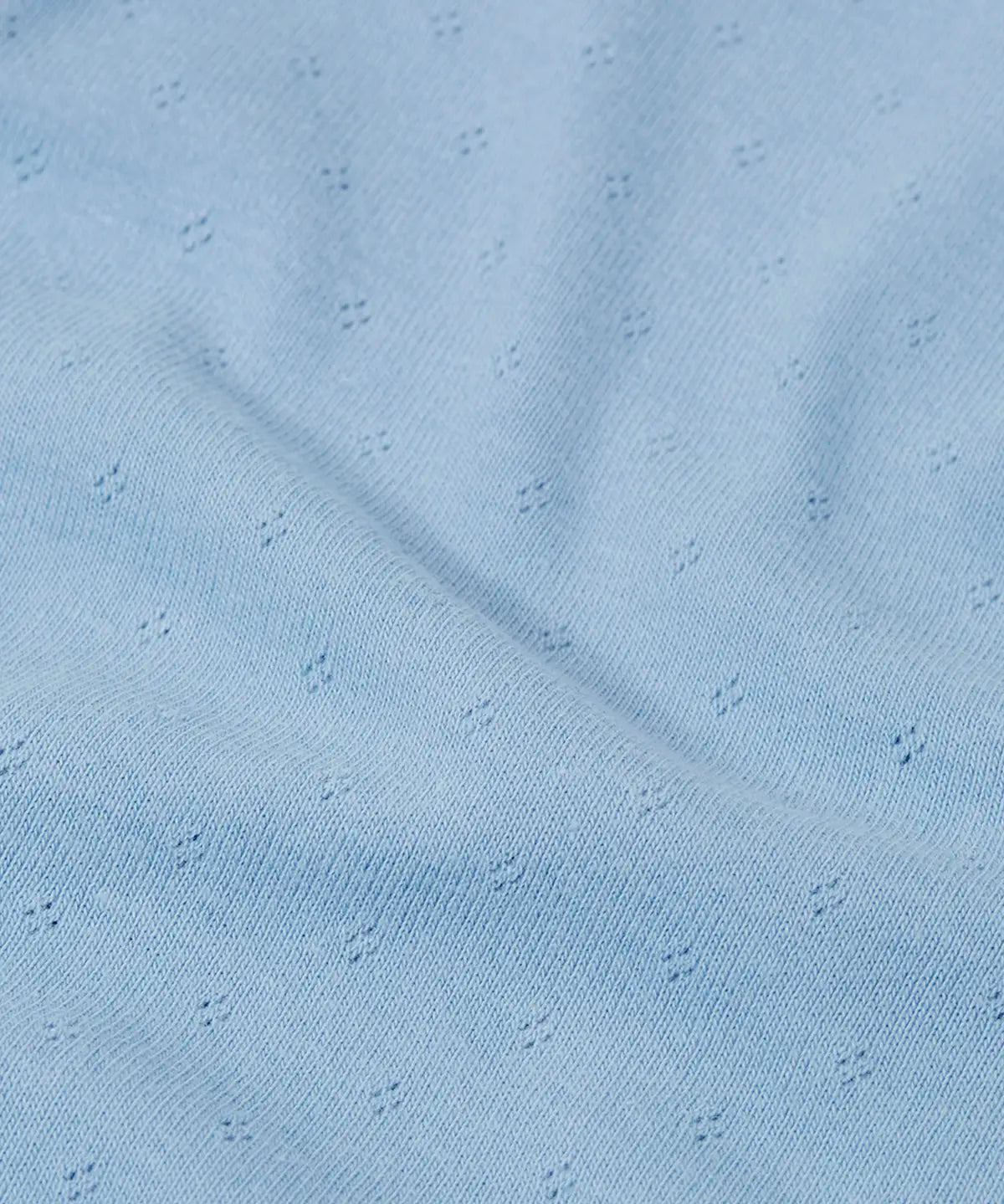 Close up of the organic cotton material of the Frugi pointelle long sleeved baby body in winter sky blue. 