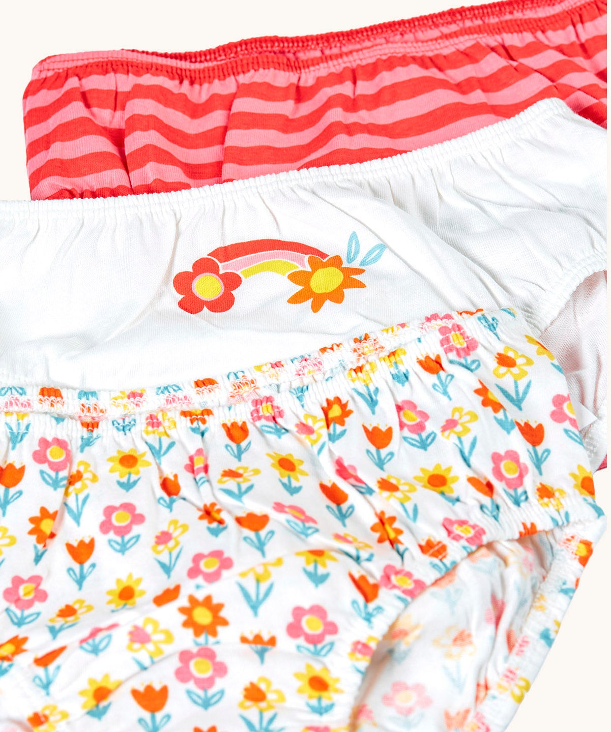 Close up of front of Frugi organic cotton briefs underwear multipack bloom flowers design. A 3 pack, one brief has an all over flower design, one is white with a rainbow flower graphic on the front and the other has a red and pink striped design.