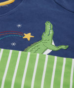 A close up of the Frugi kids Porth crocodile pyjama set showing the appliqué of a star and green crocodile with a star embroidery on the top and the green striped shorts on organic cotton fabric