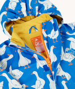A close up of the top of the orange zip opening on the Frugi cobalt blue rain jacket with all over goose print. The jacket has a yellow jersey lining and a label underneath the hanging loop inside with space to write names. 
