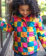 A child wearing the Frugi kids snow and ski coat in rainbow check. A multicoloured check winter coat with 2 side pockets with reflective strips on the arms