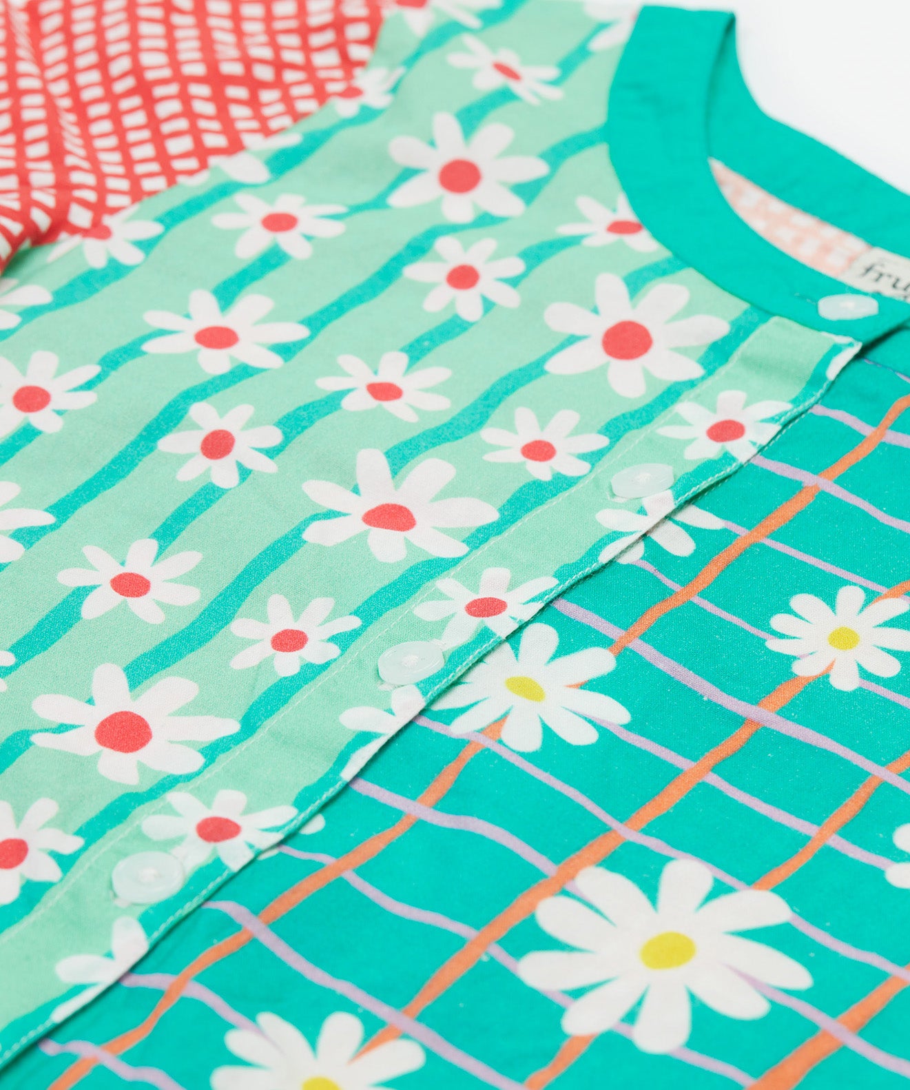 A close up of Frugi Estella Shirt, with a Rainbow Hotchpotch print, including daisies on striped green and mint backgrounds with white buttons down the middle.