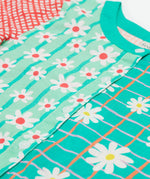 A close up of Frugi Estella Shirt, with a Rainbow Hotchpotch print, including daisies on striped green and mint backgrounds with white buttons down the middle.